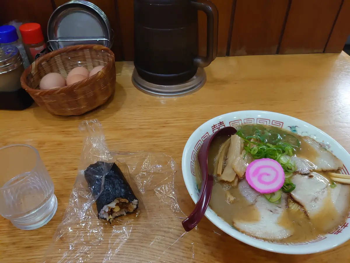 木桌上的一碗和歌山拉麵、一條用保鮮膜包著的捲壽司，以及一籃水煮蛋