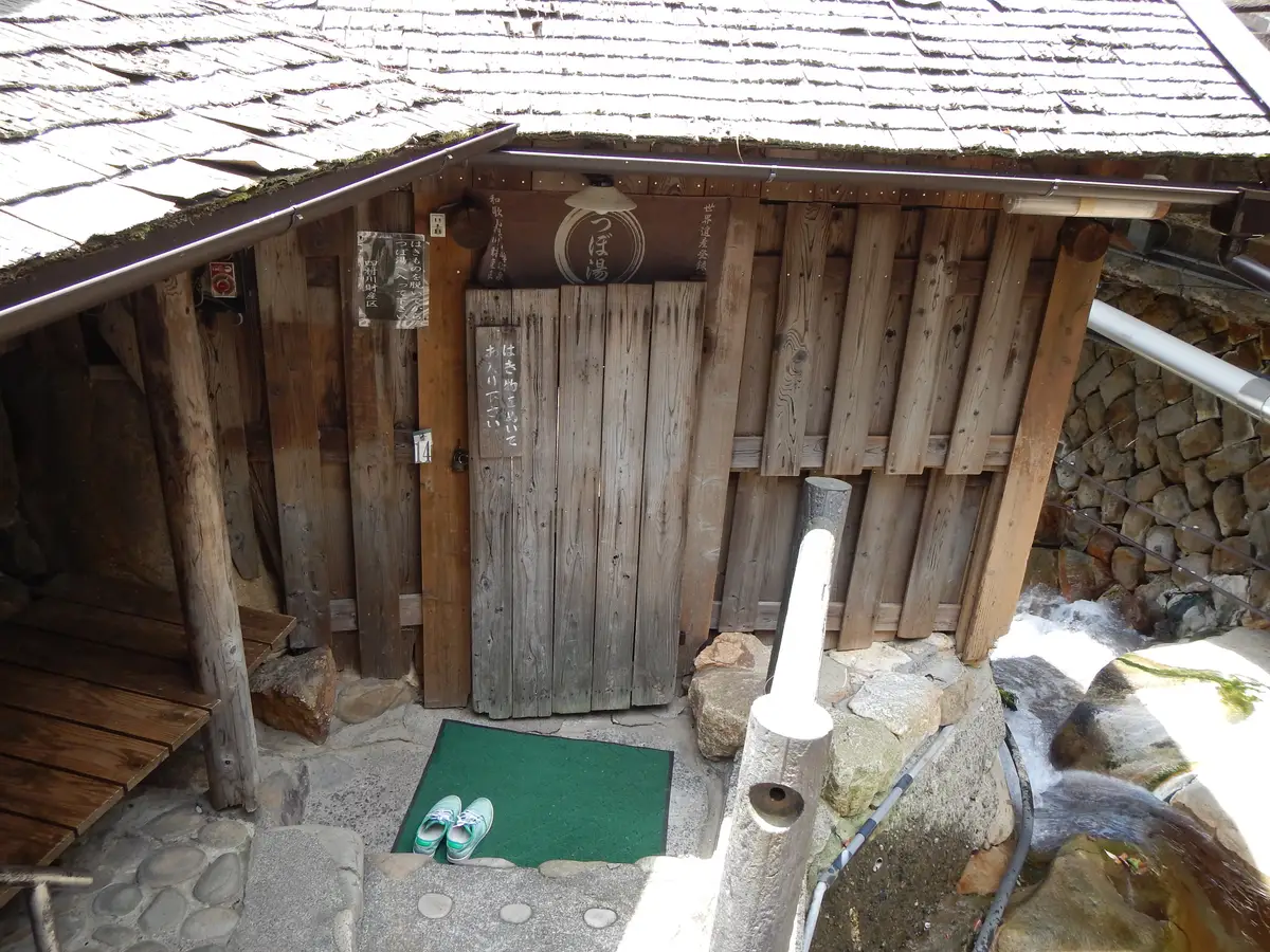 湯峰溫泉壺湯小屋掛著招牌的木門，門外放著一雙鞋