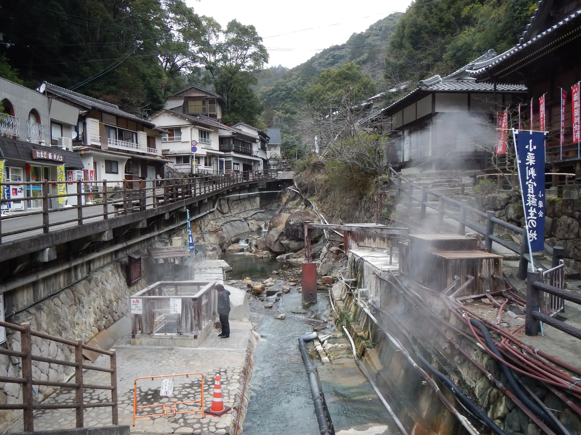 湯峰溫泉村中冒著熱氣的溪流，岸邊有煮蛋用的湯筒、旅館與寺院